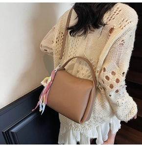 Détail d'un sac seau marron à motif litchi avec ruban à carreaux porté par un mannequin