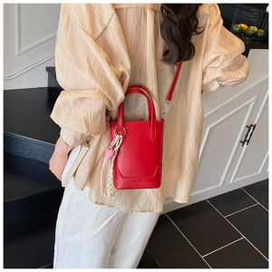 Détail du sac seau en cuir rouge porté en bandoulière avec pendentif cœur rose élégant