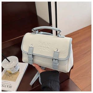 Detail of elegant two-tone faux leather crossbody bag with embossed lettering and metal buckle