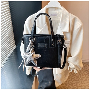 Detail of black crocodile pattern handbag with silver star charm and tassel accessory