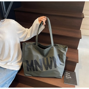 Detail view of a spacious dark green canvas tote bag with MNWM lettering on wooden stairs