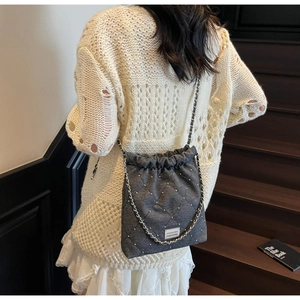 Detail of dark grey quilted denim bag with silver chain strap and drawstring closure