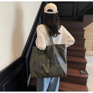 Detail shot of a large olive green canvas tote bag with MNWN lettering on model