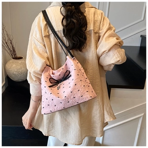 Détail du sac seau rose à texture bulles avec nœuds noirs et breloque cœur porté par le mannequin