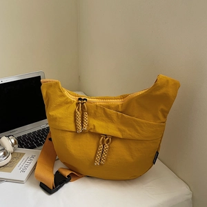 Close-up of yellow nylon crescent bag with woven zipper pulls on a white desktop