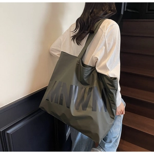 Detail of a large olive green tote bag with MNWM lettering carried by a model