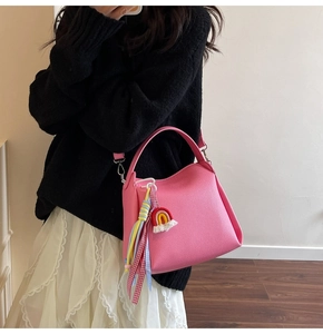 Détail du sac seau en cuir rose avec charm arc-en-ciel et sangle tissée sur modèle