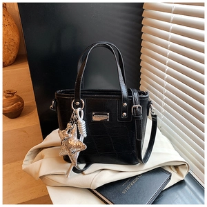 Detail of black crocodile texture tote bag with silver star charm on a beige blazer