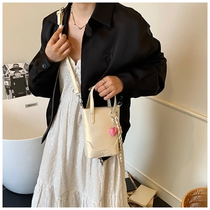 Détail du mini sac seau crème avec logo doré, breloque cœur rose et bandoulière