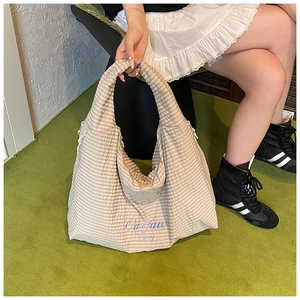Detail of beige striped canvas tote bag with blue embroidery and zipper closure