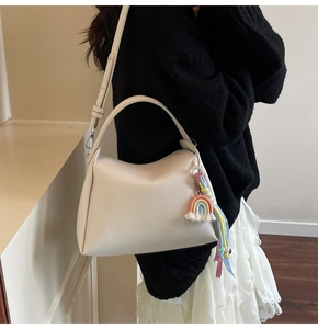 Détail d'un sac seau en cuir beige grainé avec un pendentif pompon arc-en-ciel