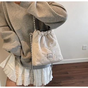 Quilted cream bucket bag with silver studs and chain strap shown on model's shoulder