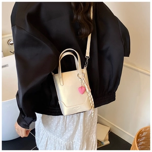 Détail d'un mini sac seau crème avec breloque cœur et bandoulière sur modèle