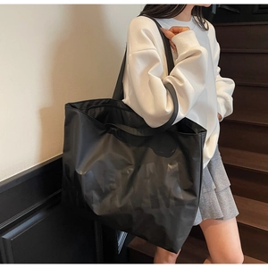 Detail of black nylon tote bag featuring subtle letter print and durable shoulder straps