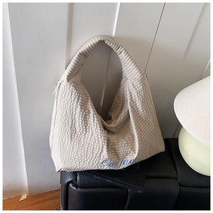 Detail of knit striped tote bag with blue embroidered text on cream textured fabric