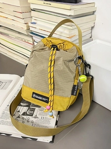 Grey checkered drawstring crossbody bag with yellow accents and a tennis racket charm