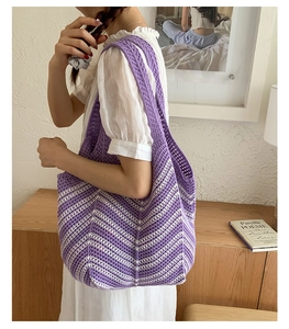 Dettaglio della borsa tote a maglia viola e bianca indossata a spalla per scala