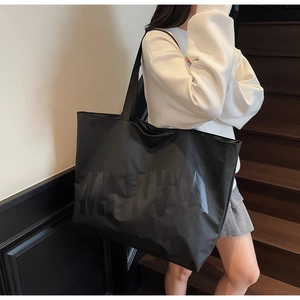 Detailed view of large black tote bag with glossy letters on glossy synthetic fabric