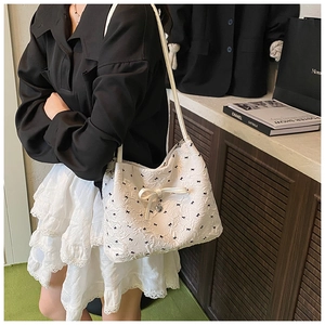 Détail du sac bandoulière en jacquard blanc avec nœuds noirs et pendentif cœur