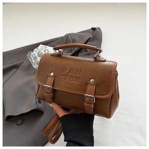 Detail showing textured brown faux leather with embossed logo and metal buckles on handbag