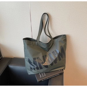 Detail shot of the olive green canvas tote bag featuring MNWM lettering on a leather sofa