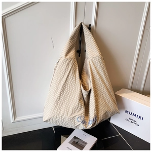 Detail view of woven check tote bag with blue embroidered text hanging on a door handle