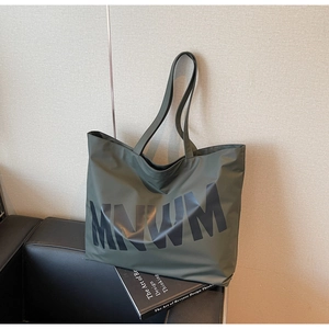 Detail of army green large capacity tote bag featuring bold MNWM lettering on a sofa
