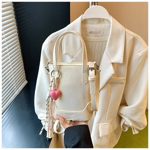 Gros plan d'un sac seau blanc avec pendentif cœur rose et pompon sur fond de veste chic
