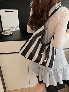 Chic black and white striped woven tote bag with leather strap shown on shoulder