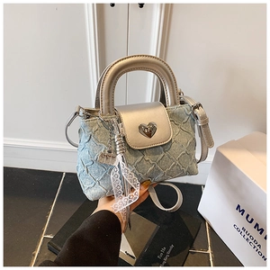 Detail of blue denim bucket bag with silver trim, heart clasp, and lace tassel charm