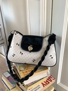 Elegante Schultertasche mit Punkten, schwarzer Schleife und Herzanhänger auf Büchern