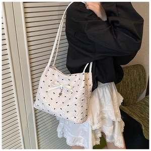 Détail du sac cabas matelassé blanc avec imprimés nœuds noirs et pendentif cœur argenté