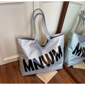 Close-up of metallic silver tote bag with MNUM lettering on a wooden floor