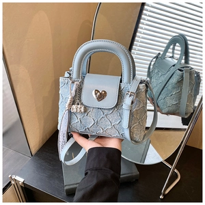 Close-up of heart-shaped metal lock and lace tassel on blue denim bucket bag