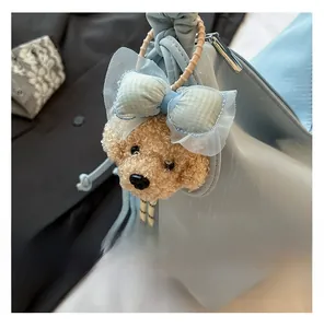Detail of light blue textured tote bag featuring a cute teddy bear plush charm with lace bow