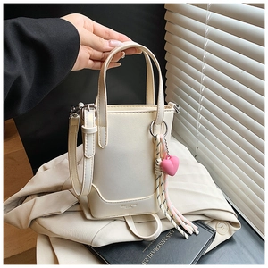 Détail du sac seau crème avec breloque cœur et pompon montrant la texture du cuir