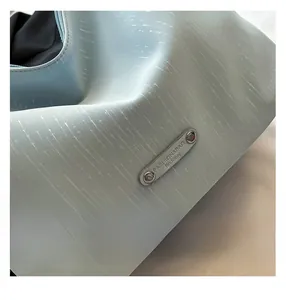 Detail of light blue textured tote bag with silver logo plaque and smooth zipper closure