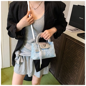 Detail of light blue textured crossbody bag with silver heart buckle and lace pendant charm
