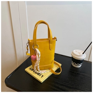 Détail d'un mini sac seau jaune avec un pendentif cœur rose et un cordon en coton tressé