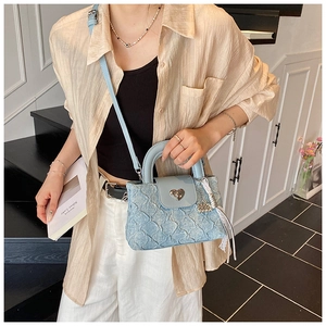 Detail of light blue textured crossbody bag with silver heart buckle and pearl charm