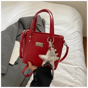 Detail of red crocodile texture handbag with silver star pendant and long shoulder strap