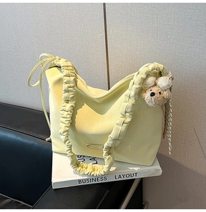 Detail of cream yellow cloud bag with ruffled shoulder strap and plush bear charm