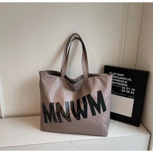 Detail of spacious beige tote bag with black MNWM lettering on marble surface