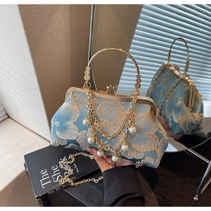 Dettaglio del ricamo floreale blu con nappa di perle e manico in metallo dorato sulla borsa