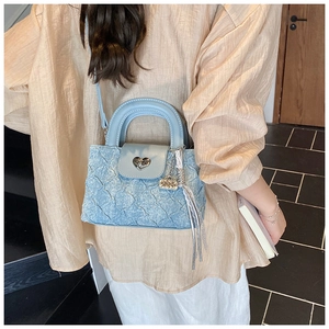 Detail of light blue textured denim bucket bag with silver heart clasp and fringe