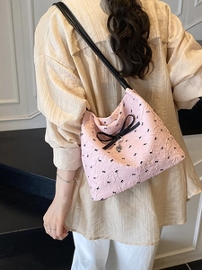 Sac à épaule rose avec nœuds noirs et pendentif cœur, porté par un mannequin pour un look chic