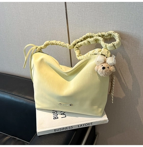 Detailed view of yellow pleated shoulder bag with cute plush bear charm and metal logo