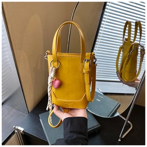 Détail du sac seau jaune avec breloque cœur rose et sangle tissée sur une coiffeuse
