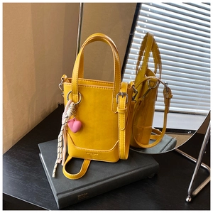 Détail du sac seau jaune avec pendentif cœur et corde tressée sur un livre sombre