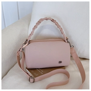 Detail of light pink nylon crossbody bag with ruffled handle on a soft cream sofa
